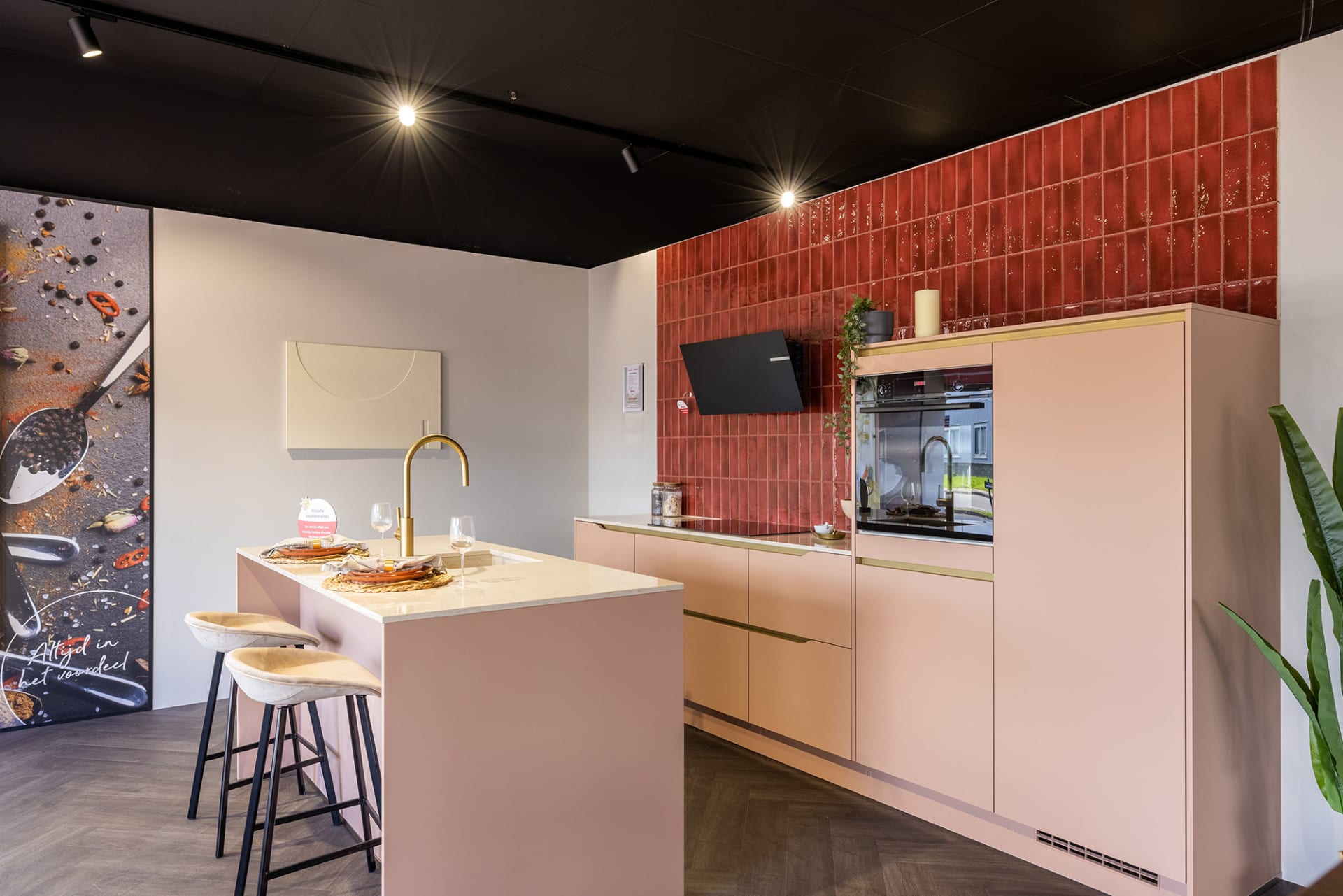 Poederroze keukenopstelling met rode tegelwand en wit kookeiland in de Kitchen4All-winkel