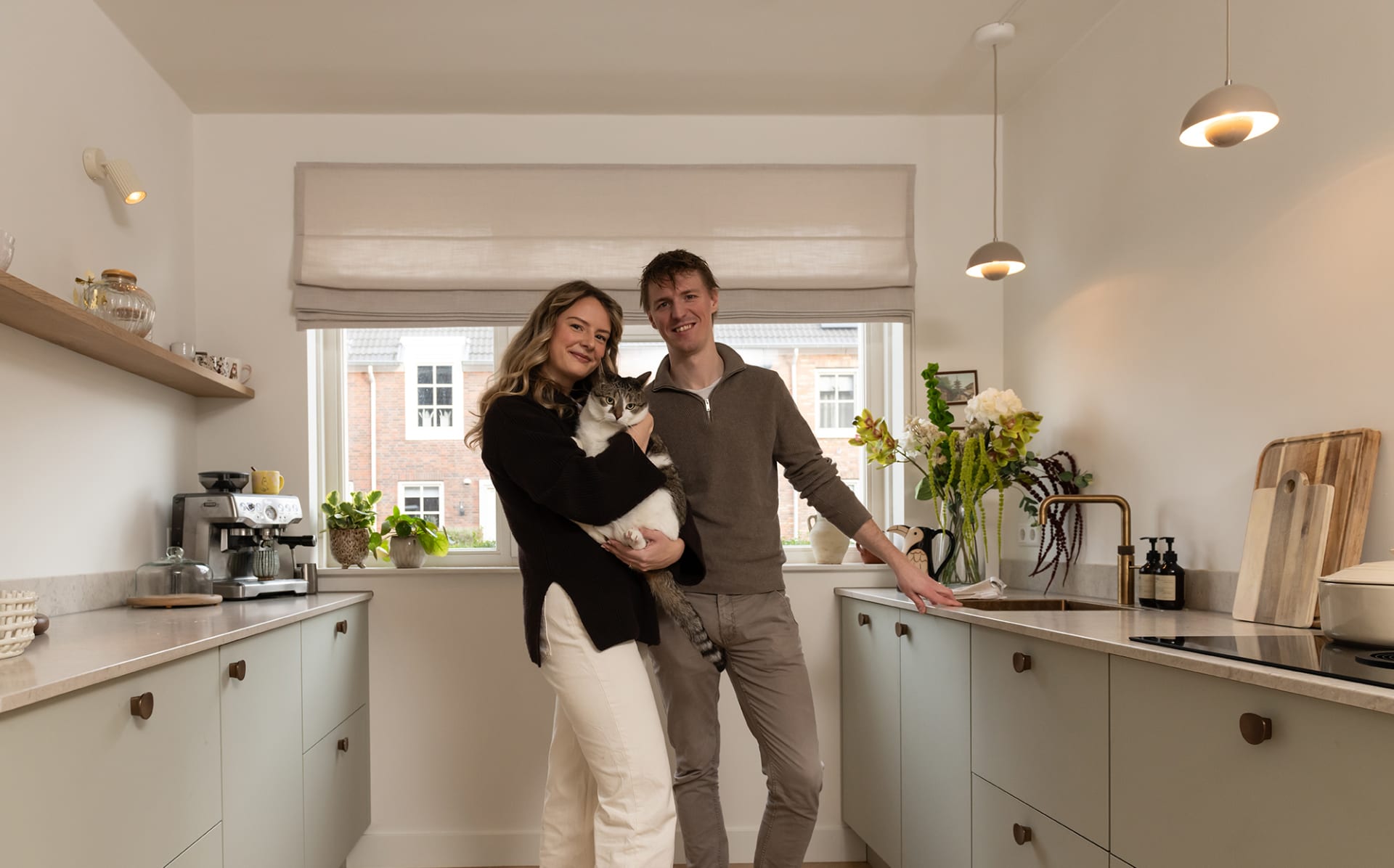 Maaike en Tijs met hun kat in hun lichte keuken met zachtgroene fronten