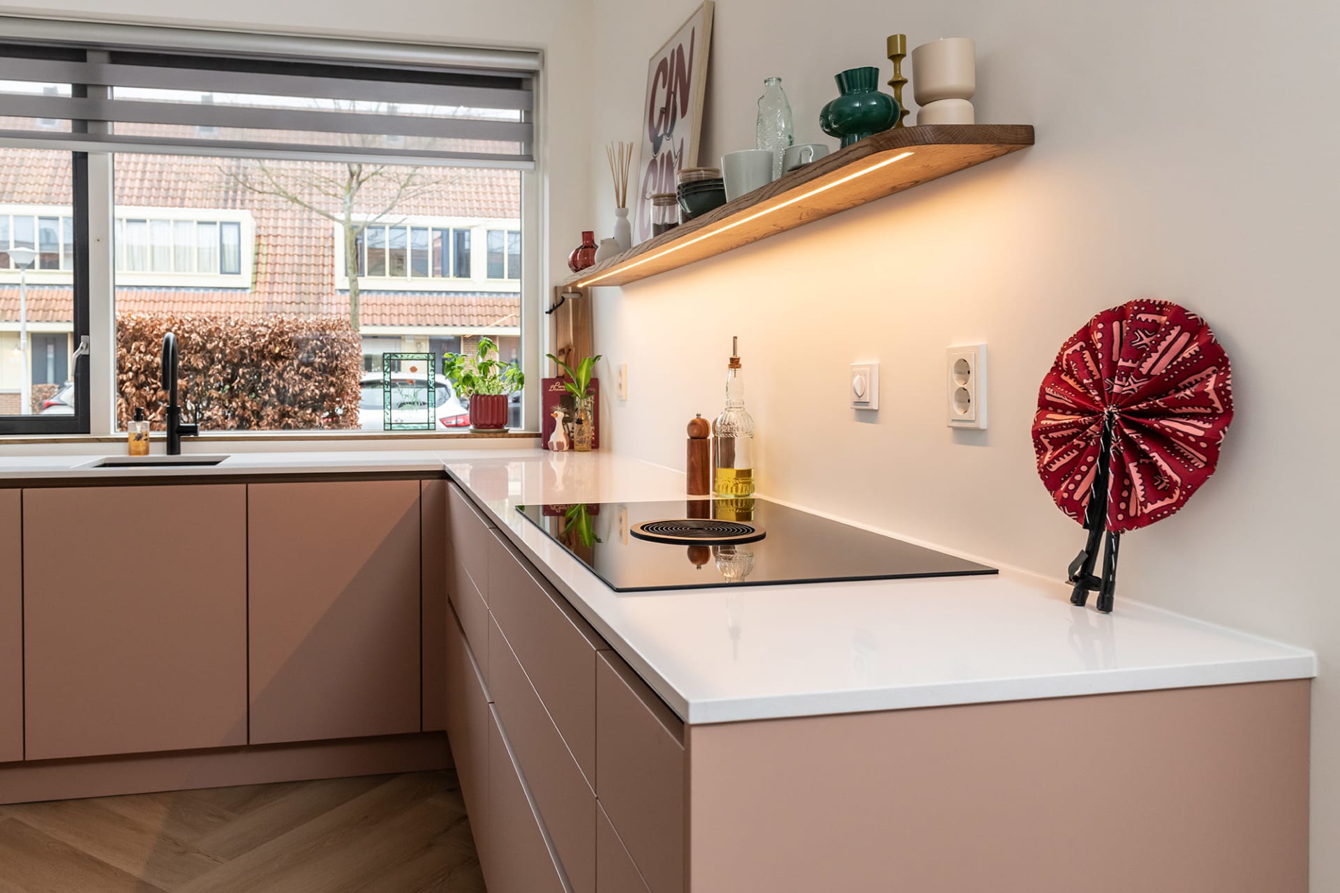 Koraalroze hoekkeuken met wit werkblad en visgraatvloer in een woonhuis