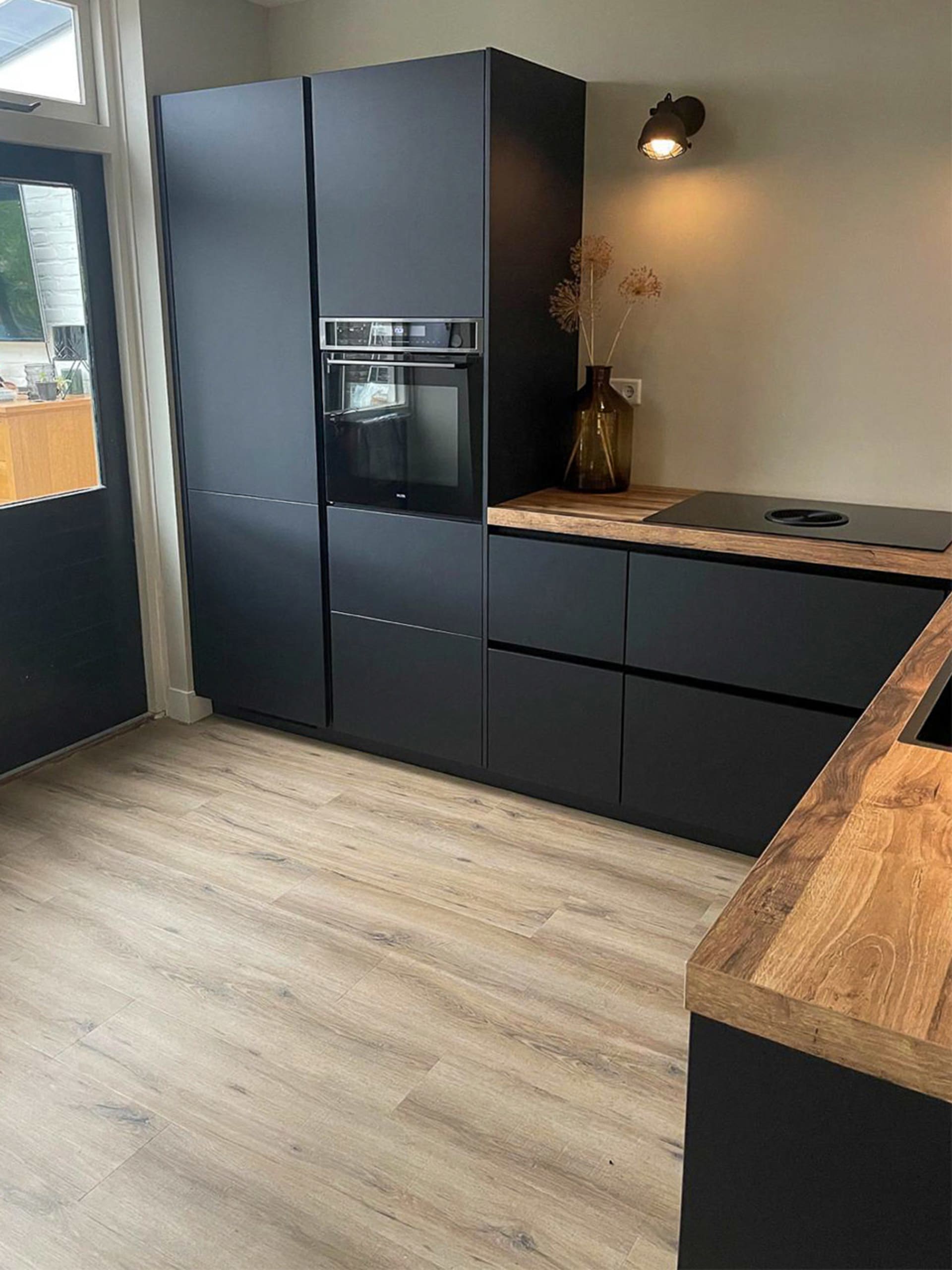 Zwarte hoekkeuken met houten werkblad in een woonkeuken