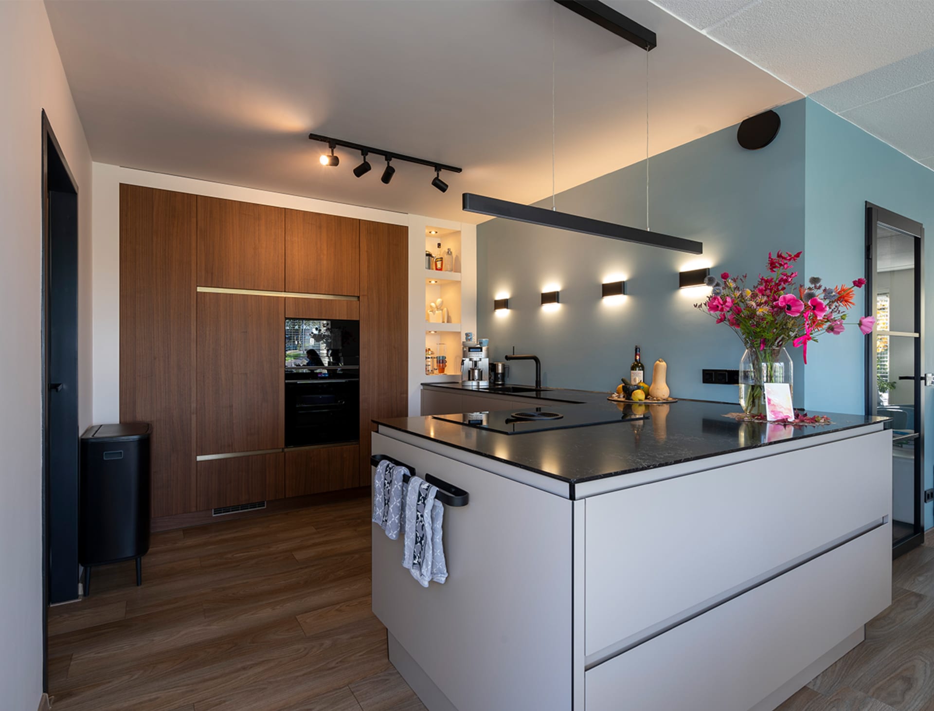 Wit kookeiland met notenhouten kastenwand en bloemen in een woonkeuken