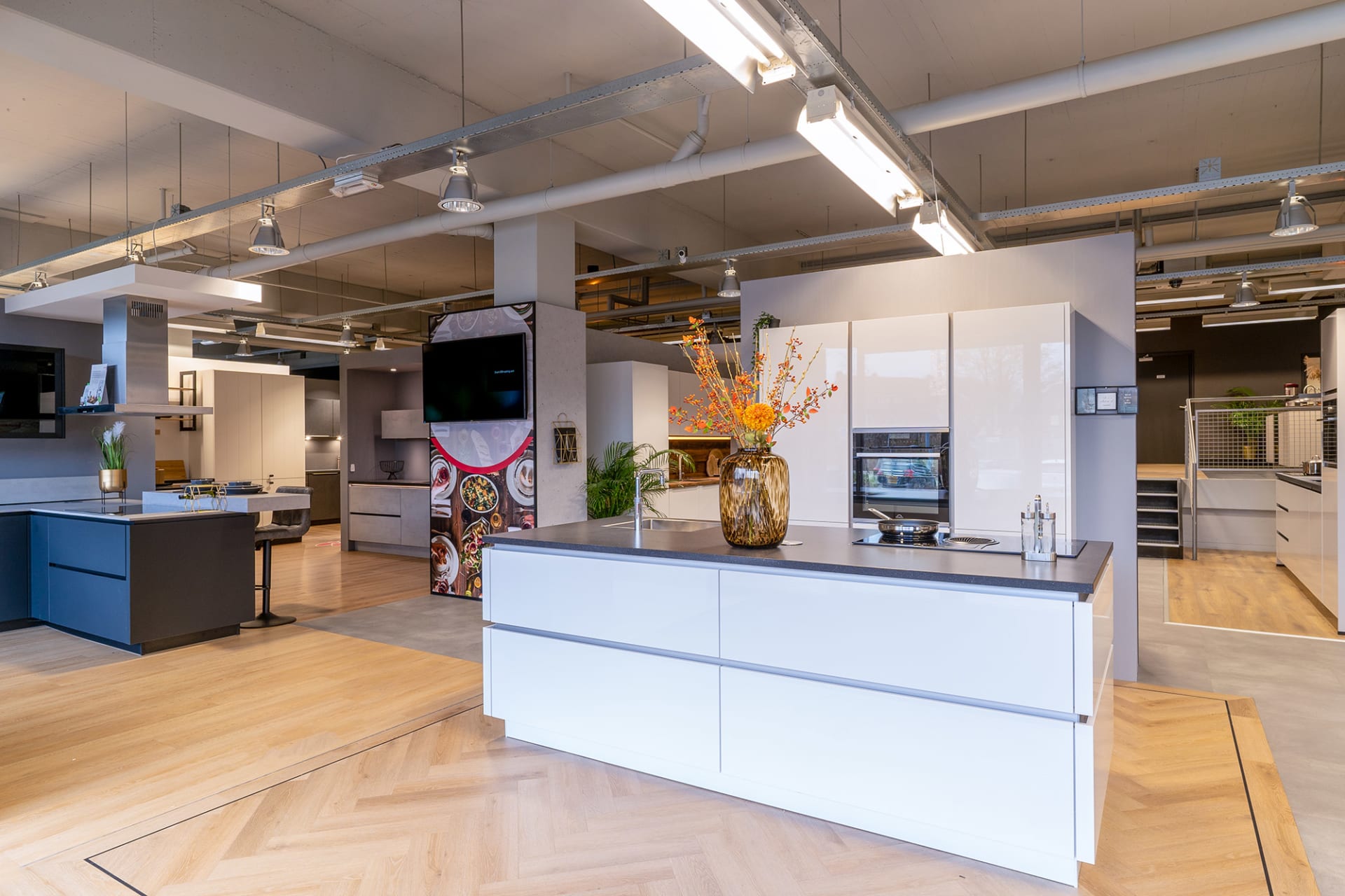 Ruime Kitchen4All-winkel met wit kookeiland en keukenopstellingen op een visgraatvloer