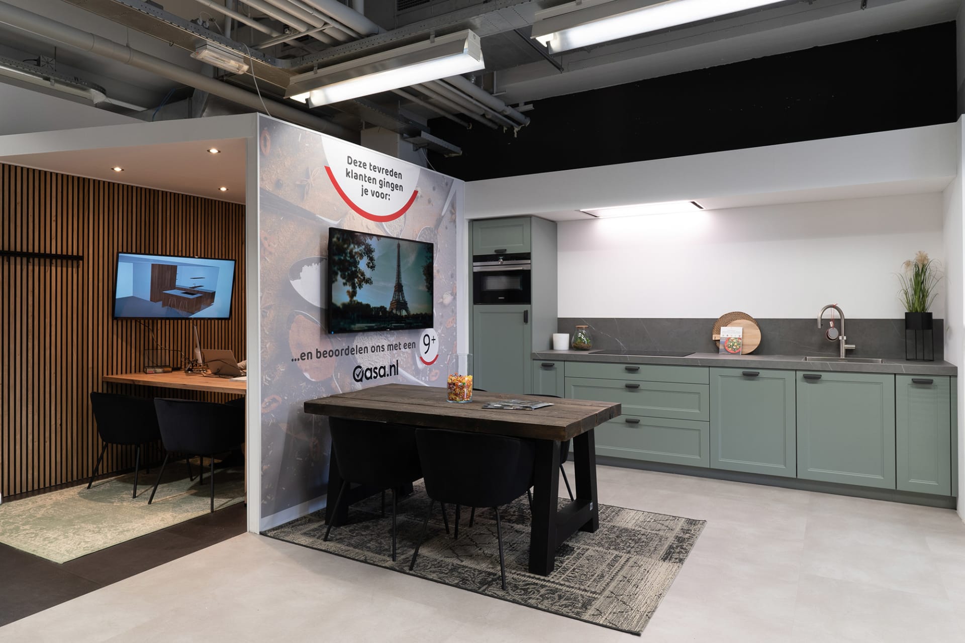 Advieshoek met houten tafel, saliegroene keukenopstelling en een 3D-ontwerp op een scherm in de Kitchen4All-winkel