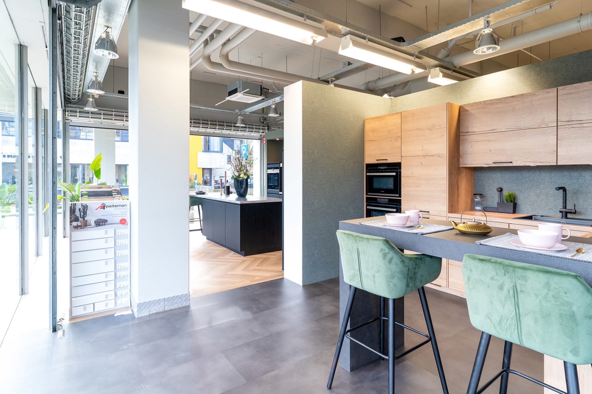 Gedekt bareiland met groene barkrukken en licht-eiken kastenwand in de Kitchen4All-winkel
