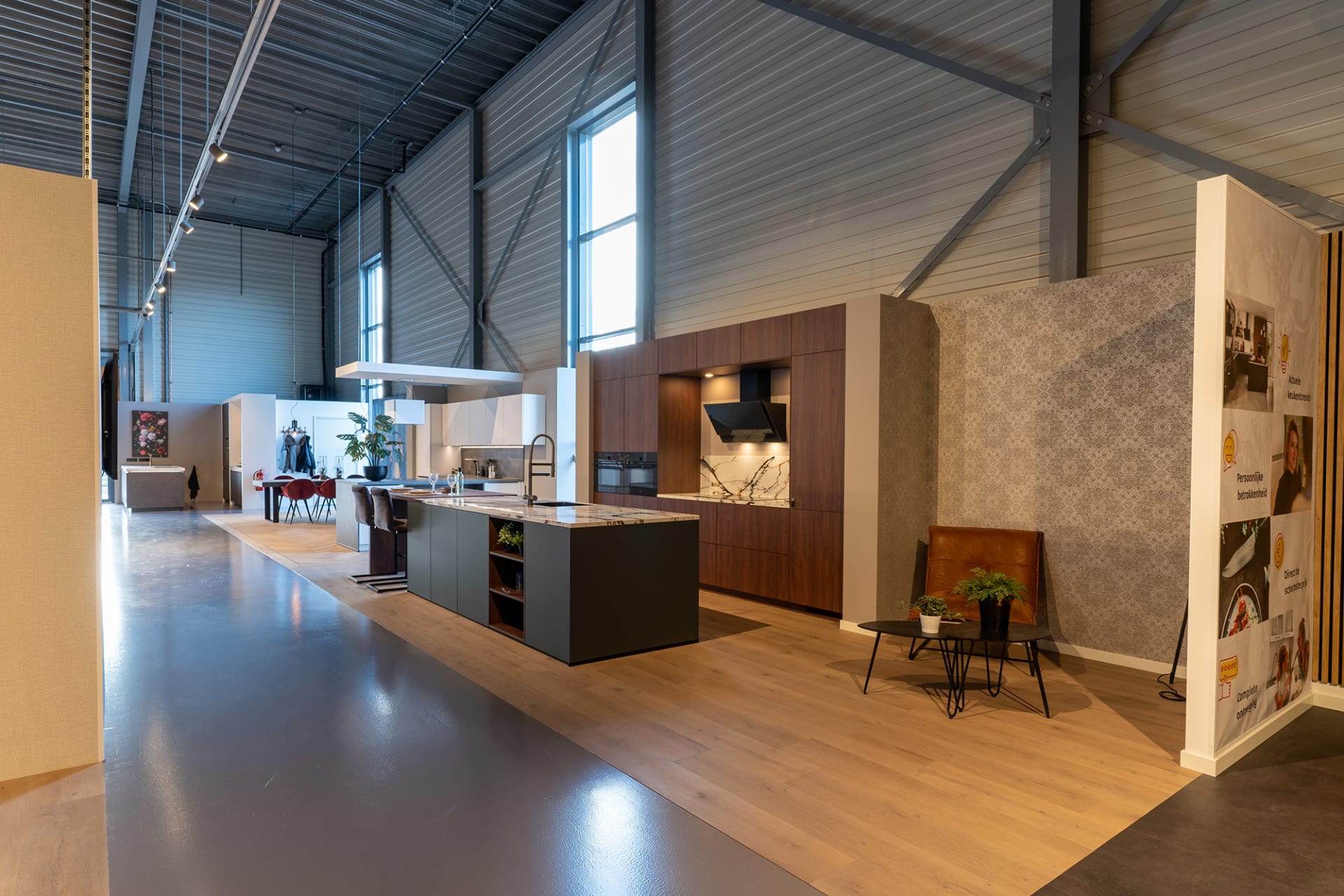 Zichtlijn door de Kitchen4All-winkel met een antracietgrijs eiland en notenhouten keukenwand