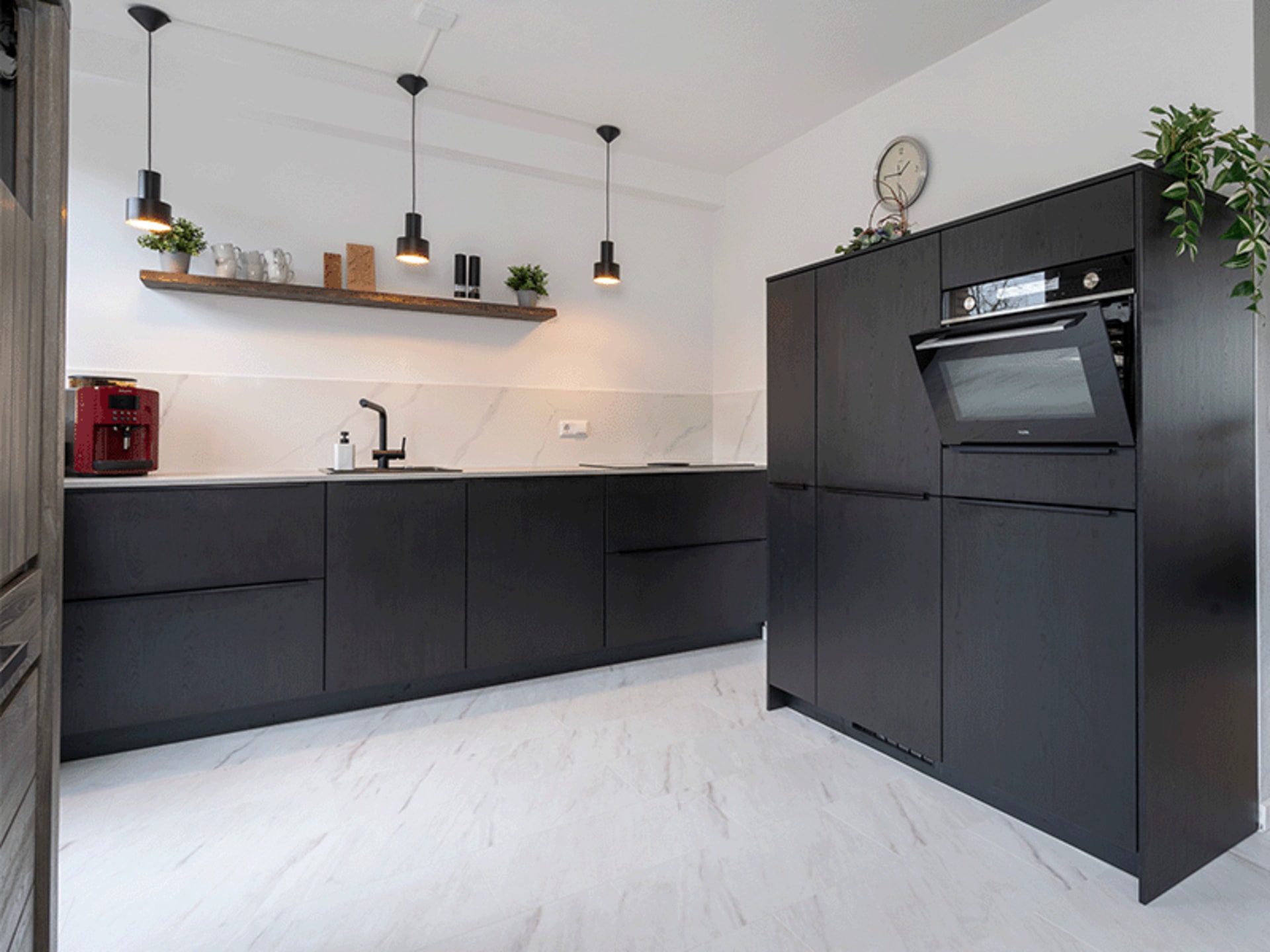 Zwarte keuken met houten wandplank en inbouwoven in een woonkeuken