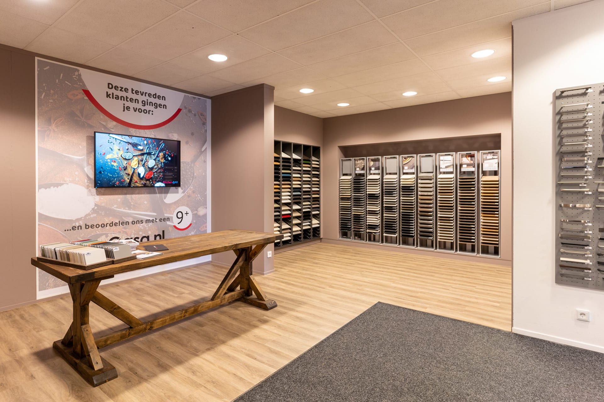 Stalenwand met fronten en werkbladen en een houten zitbank in de Kitchen4All-winkel