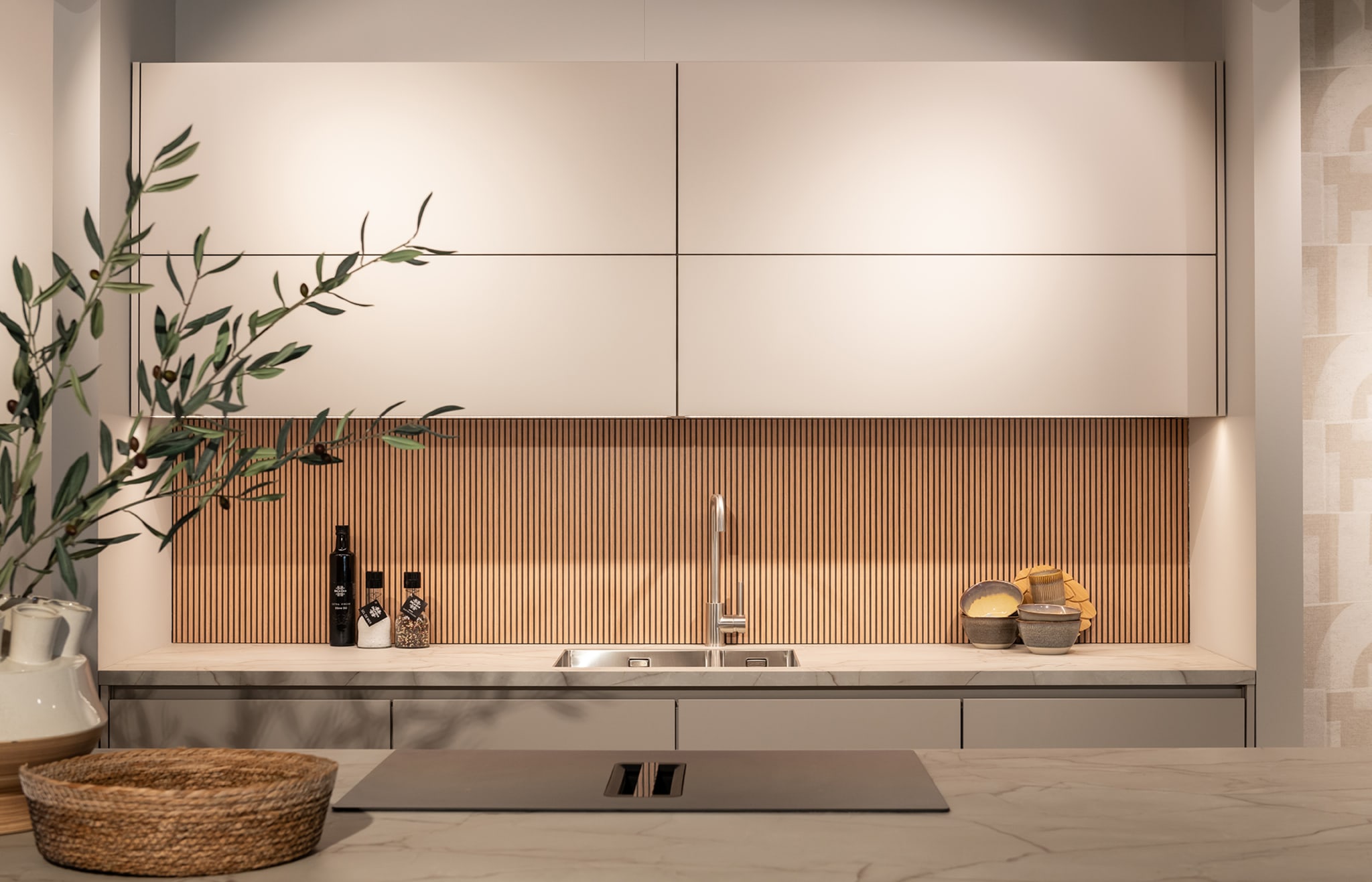 Een moderne keuken met beige kasten, een houtlook achterwand en een kookeiland met geïntegreerde afzuiging.