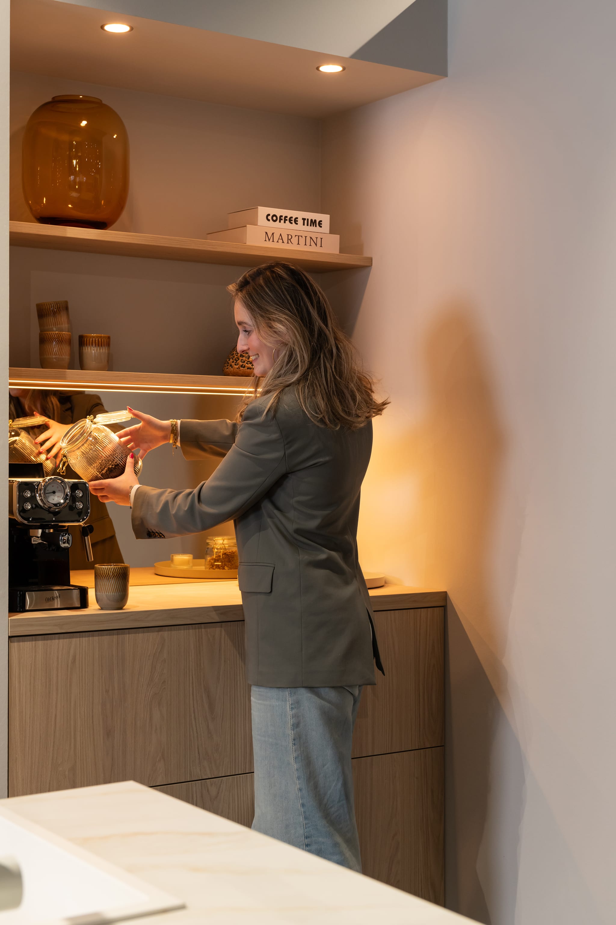 Een vrouw zet koffie in een moderne Kitchen4All keuken met houtlook fronten en een marmerlook werkblad.