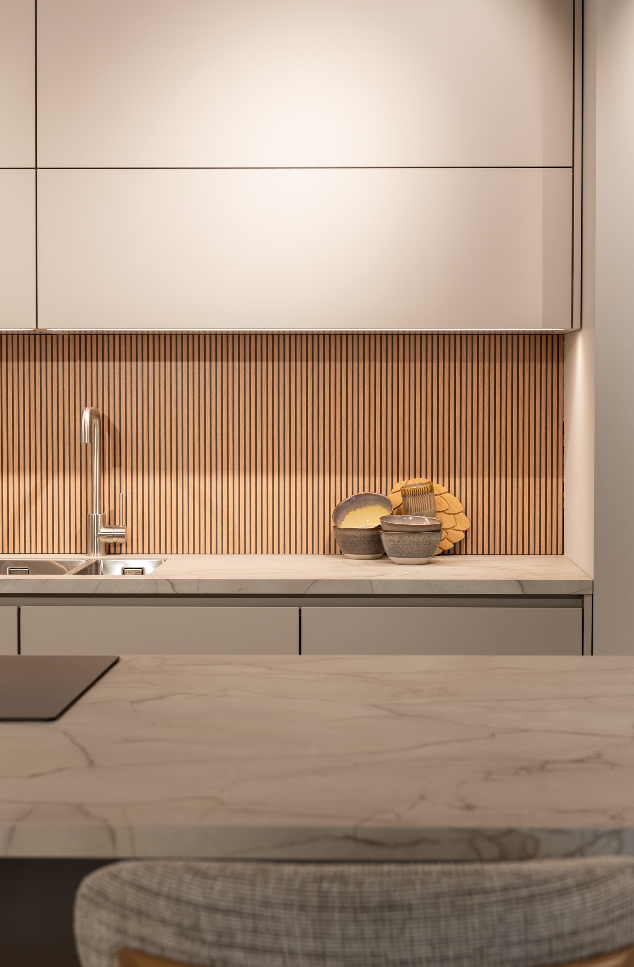 Moderne Nordic warm keuken met greeploze fronten, houten achterwand en een stijlvol marmerlook kookeiland.