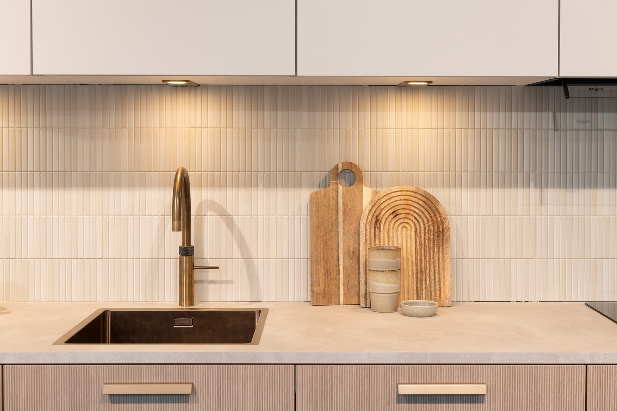 Een Japandi soft keuken met houtlook composiet werkblad, ribbel fronten en gouden kraan.
