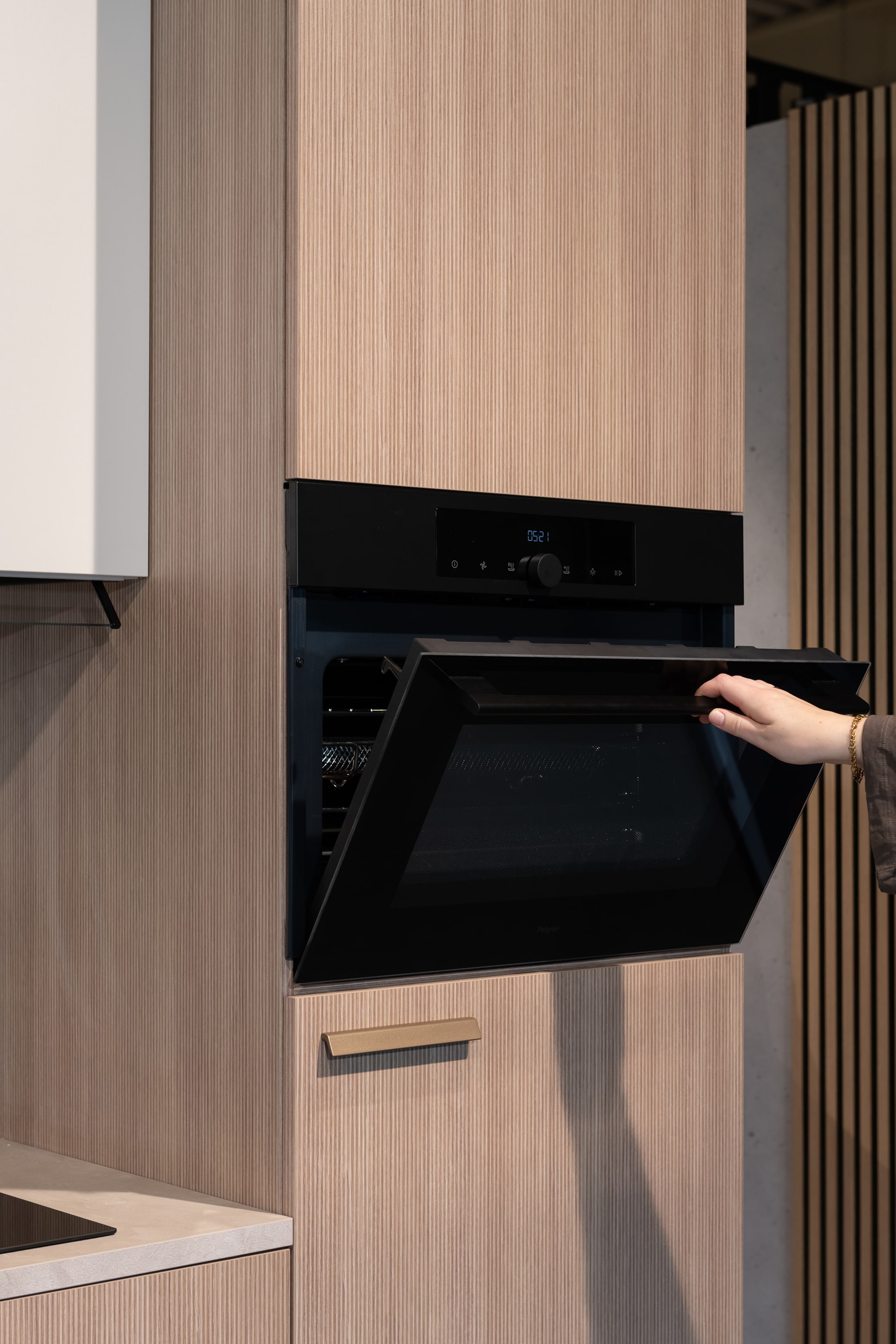 Een hand opent de zwarte oven in een moderne Japandi soft keuken met houtlook fronten.