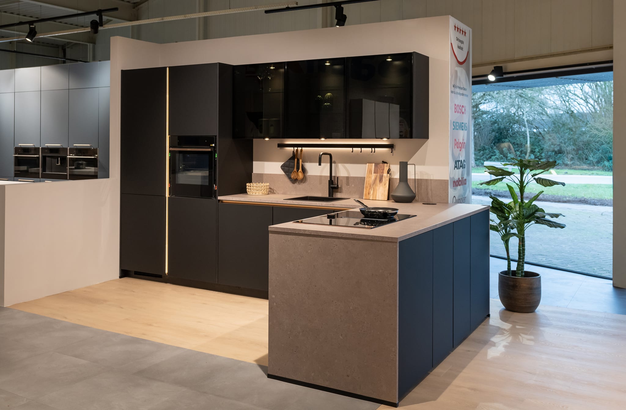 Moderne Kitchen4All keuken met matzwarte fronten, greeploos design en een kookeiland met betonlook composiet werkblad.