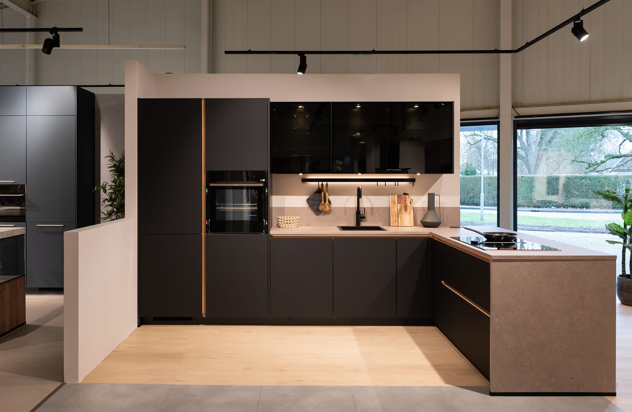 Moderne L-keuken met matzwarte greeploze fronten, een houtlook werkblad en zwarte accenten.