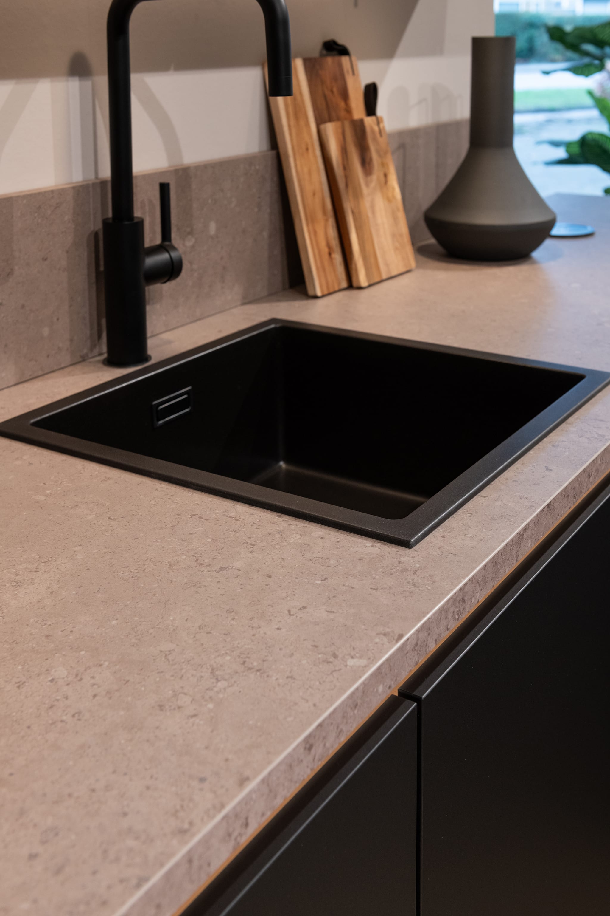 Moderne Kitchen4All keuken met greeploze zwarte fronten en een composiet betonlook werkblad met zwarte spoelbak.