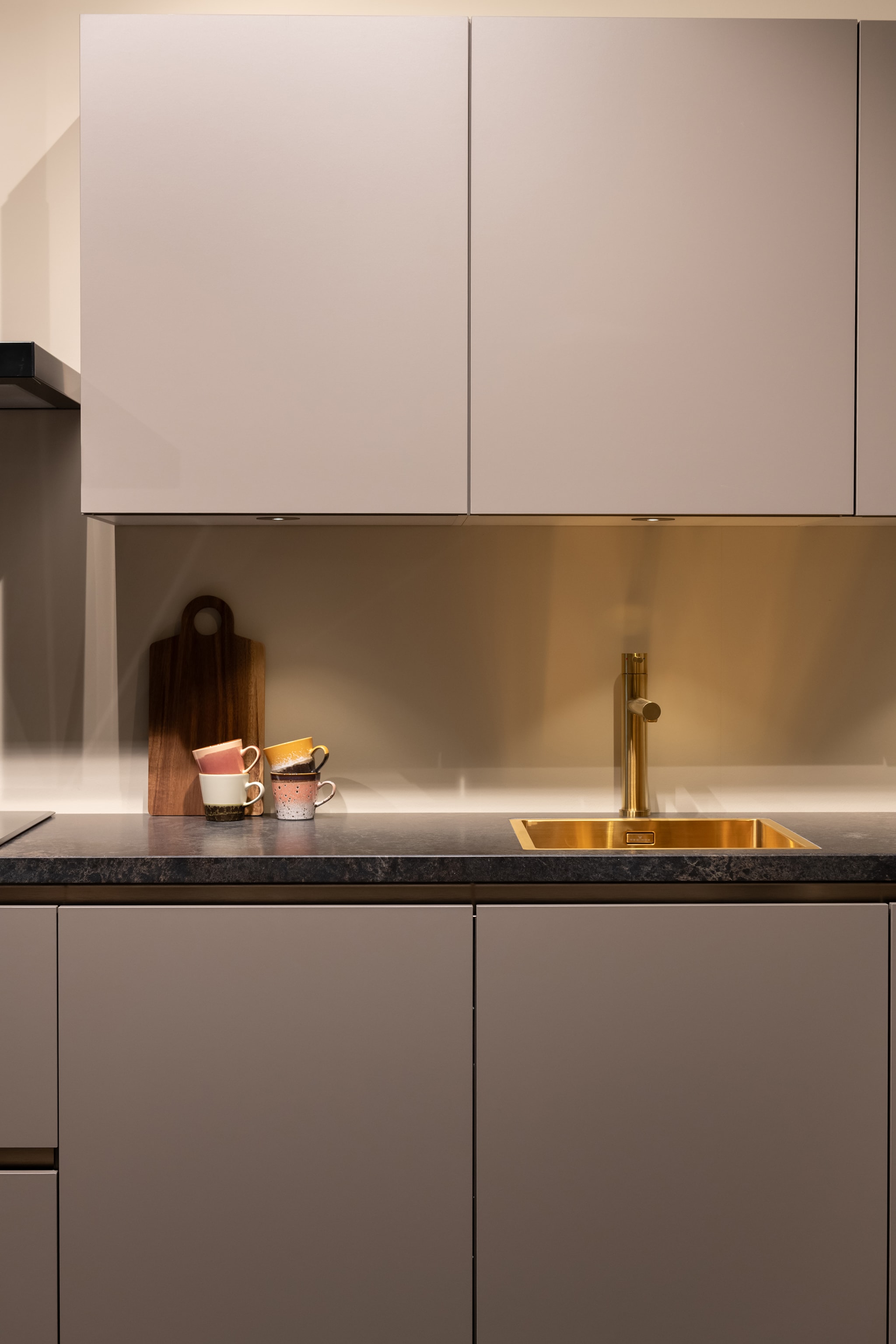 Moderne Kitchen4All keuken met matte beige/taupe fronten, donkergrijs composiet werkblad en gouden kraan.