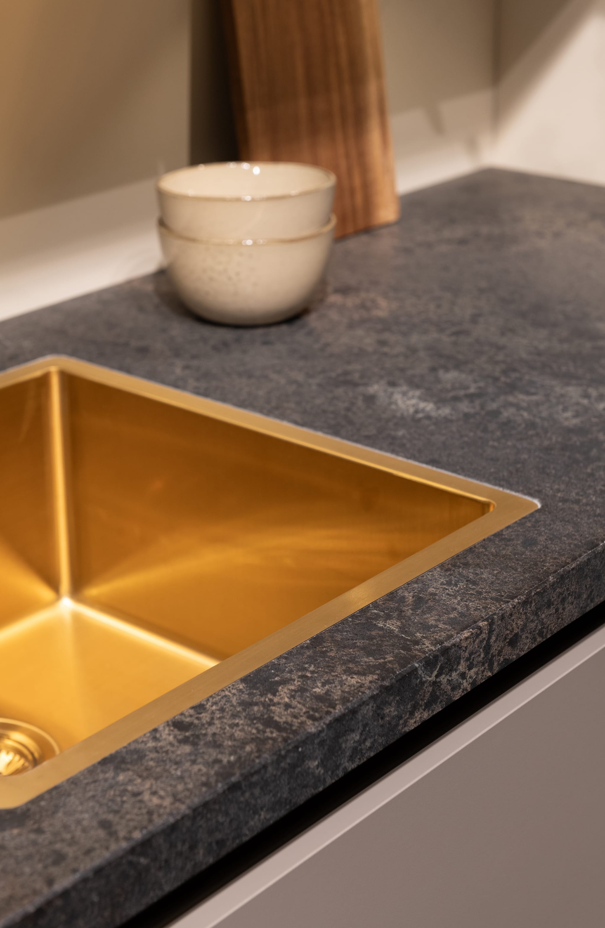 Een close-up van een moderne Kitchen4All keuken met een donker composiet werkblad en gouden spoelbak.
