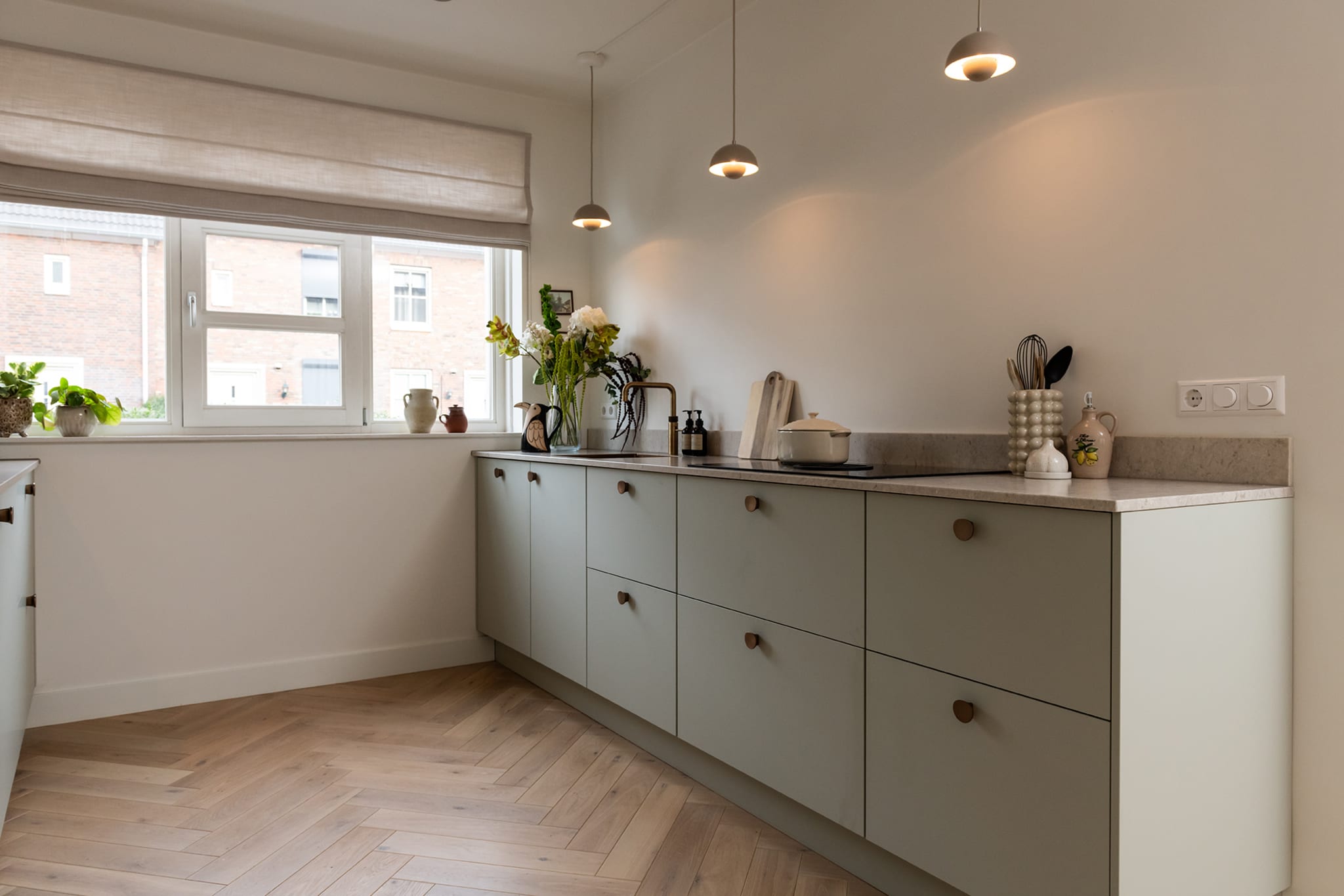 Saliegroene Scandinavische keuken met messing greepjes, hanglampen en een houten vloer