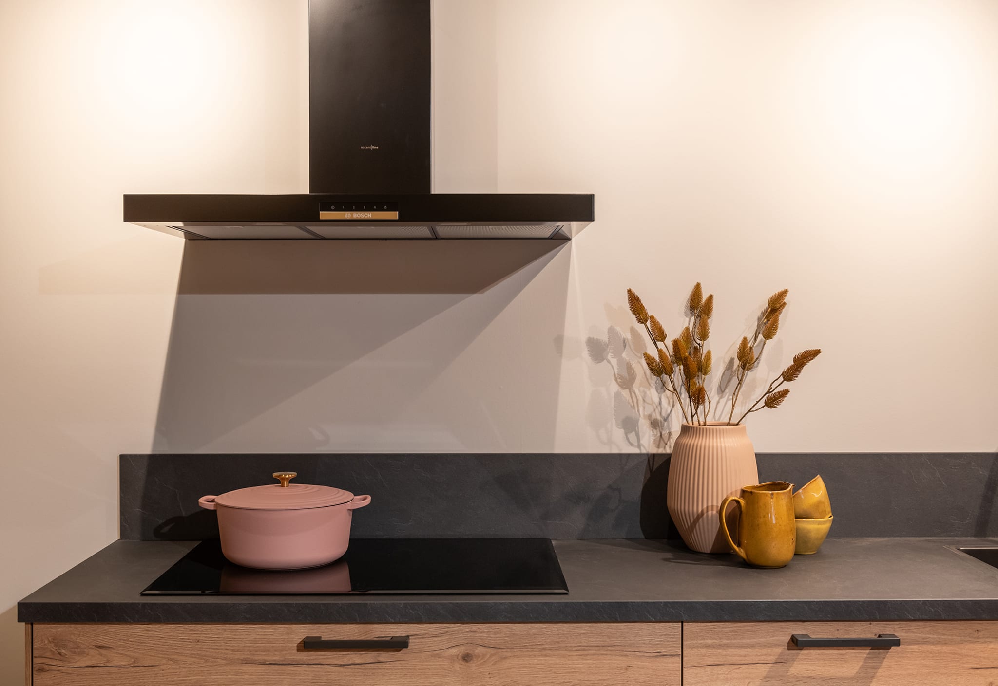 Moderne rechte keuken met houtlook fronten, donker composiet werkblad en zwarte afzuigkap.