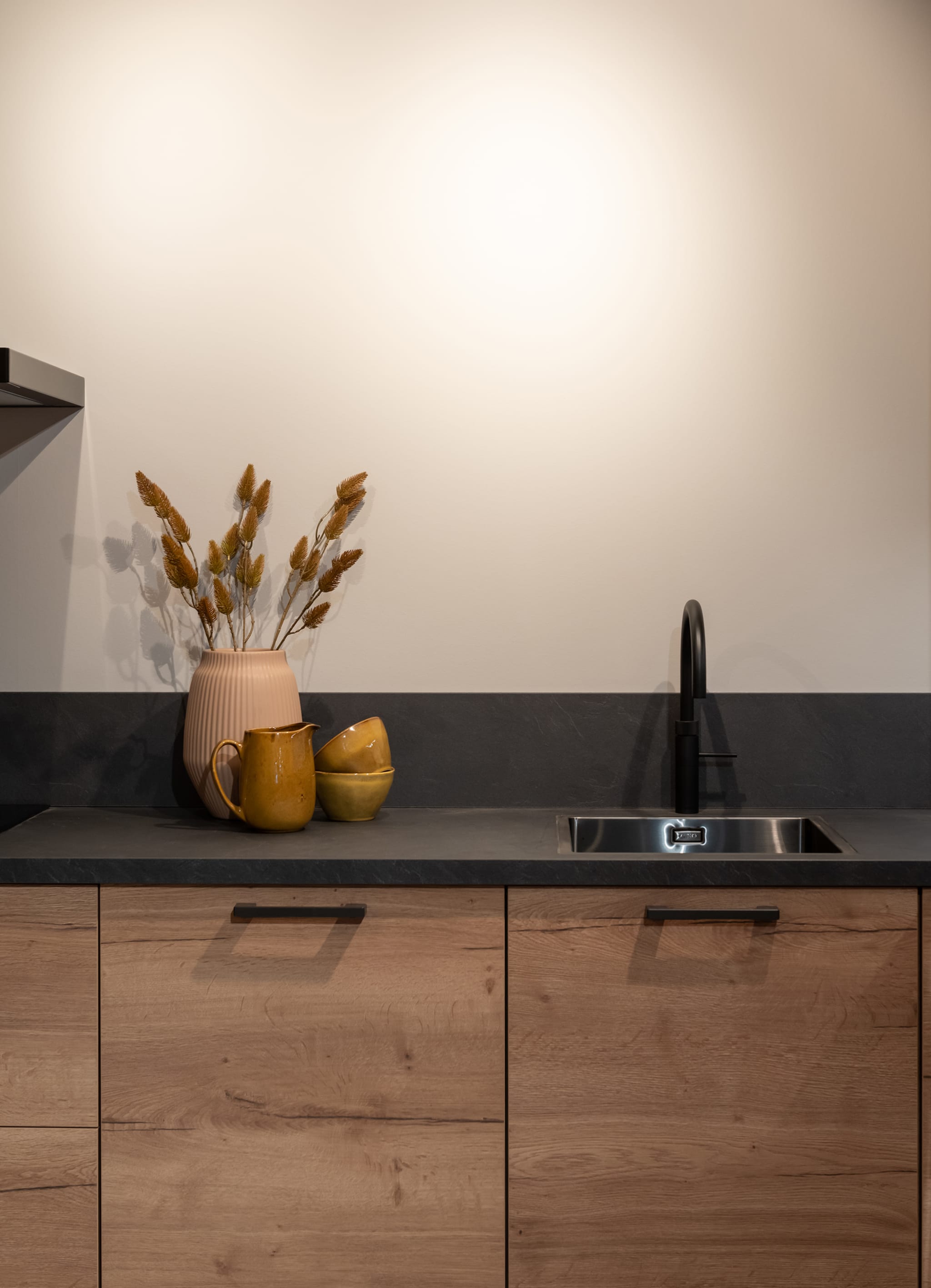 Een kleine, moderne Kitchen4All keuken met houtlook fronten, donker composiet werkblad en zwarte handgrepen.
