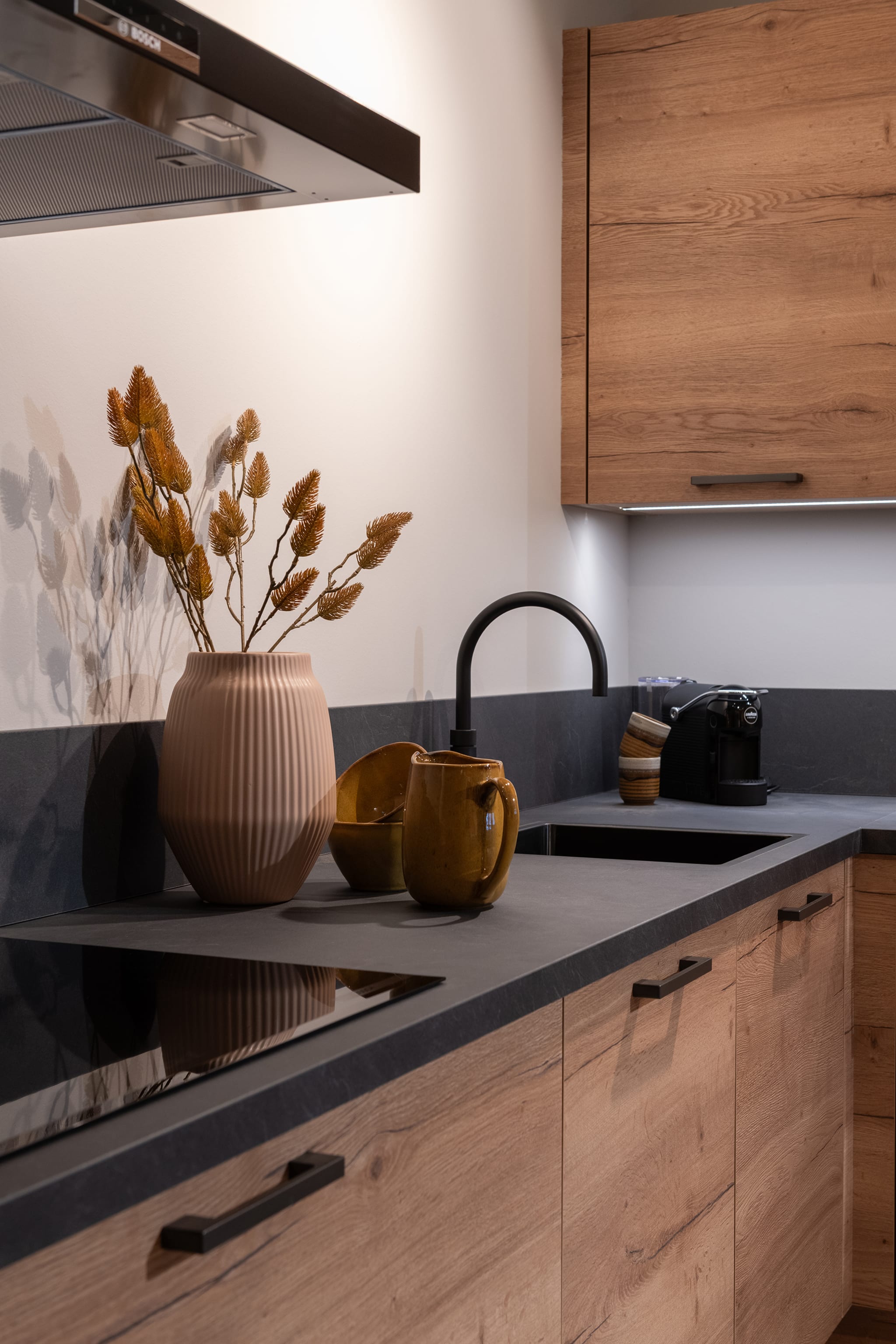 Moderne rechte Kitchen4All keuken met houtlook fronten, donker composiet werkblad en zwarte handgrepen.