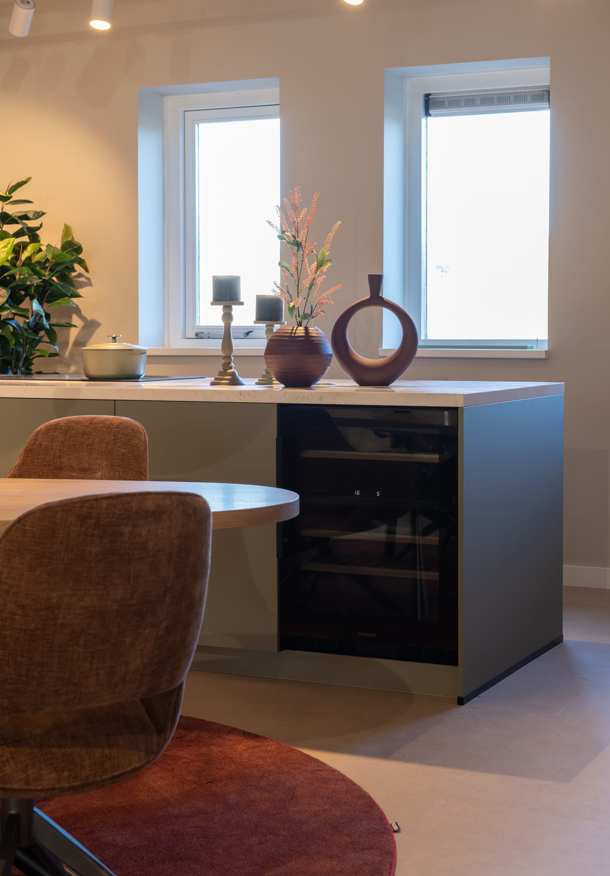 Moderne greeploze eilandkeuken van Kitchen4All met matgrijze fronten, wit composiet werkblad en geïntegreerde wijnkoeler.