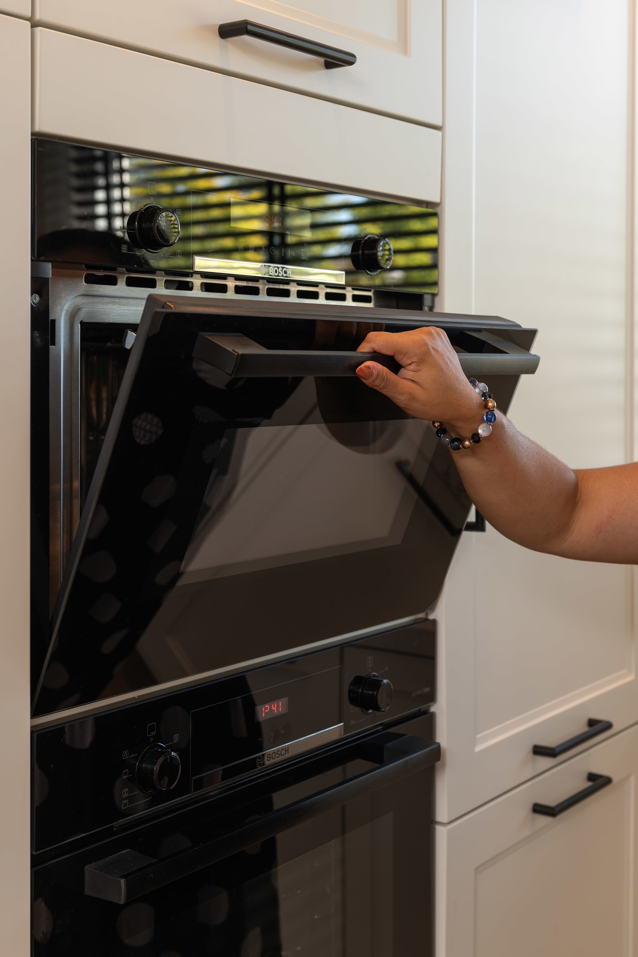 Hand opent de oven in de witte kastenwand, met de combi-oven eronder en zwarte grepen