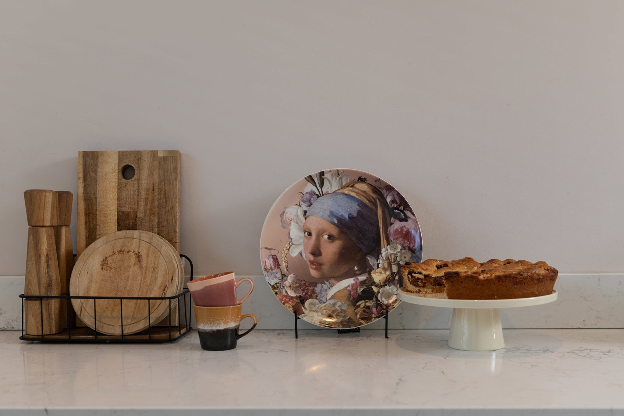 Appeltaart op een taartschaal naast houten planken en een decoratief bord op het marmerlook werkblad