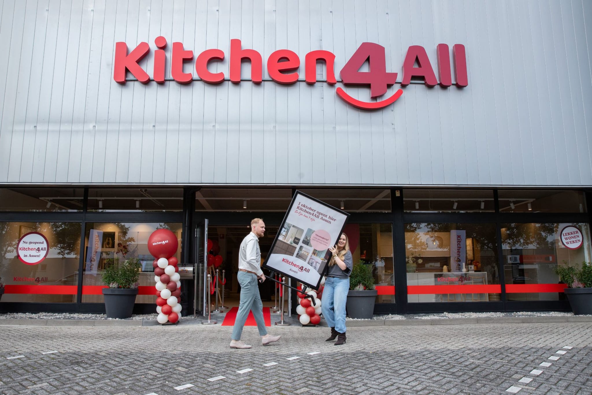 Twee medewerkers van Kitchen4All Assen dragen een bord voor de winkel aan de Zeilmakerstraat