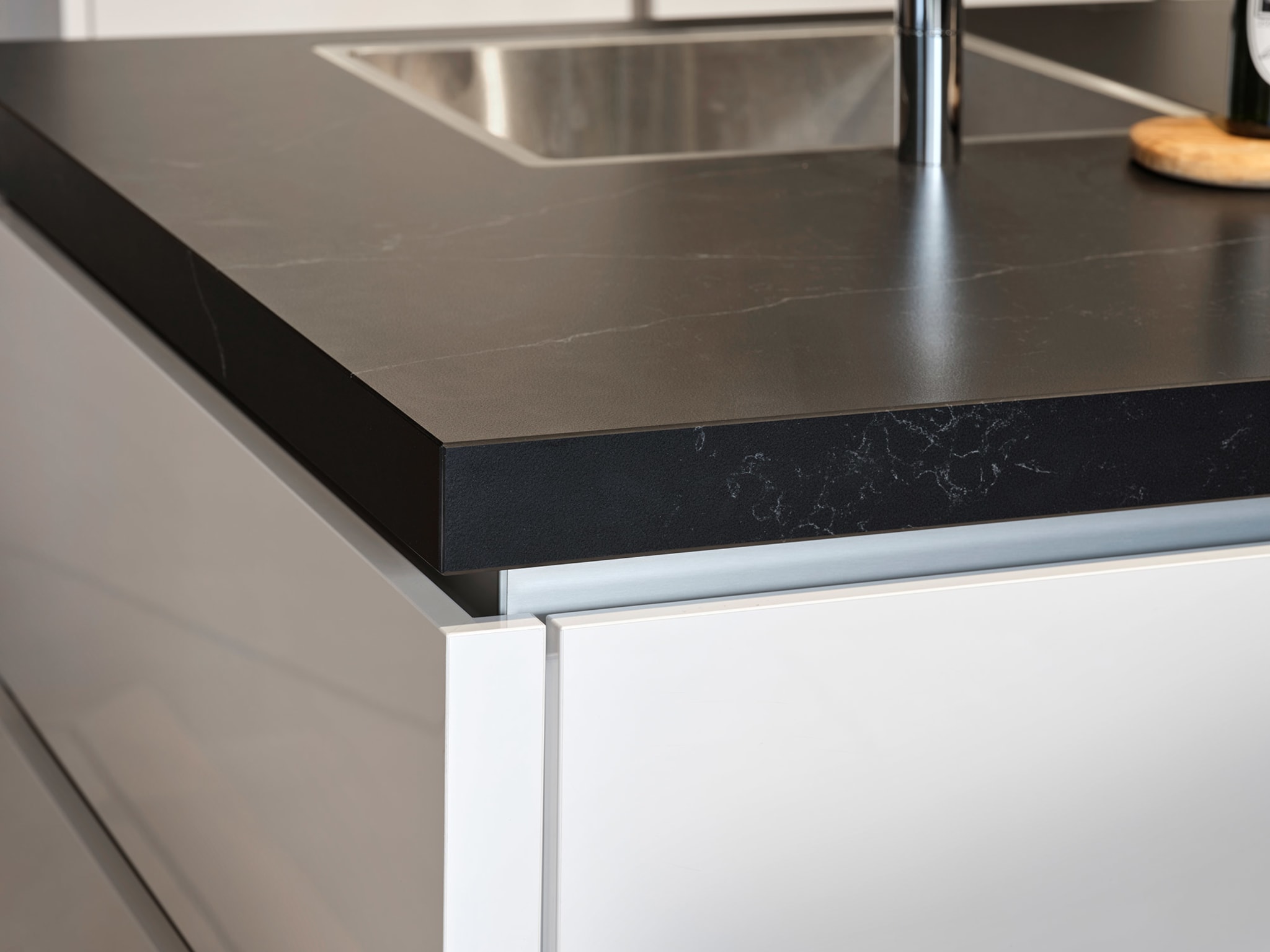 Close-up van een modern Kitchen4All kookeiland met een zwart composiet werkblad en witte greeploze fronten.
