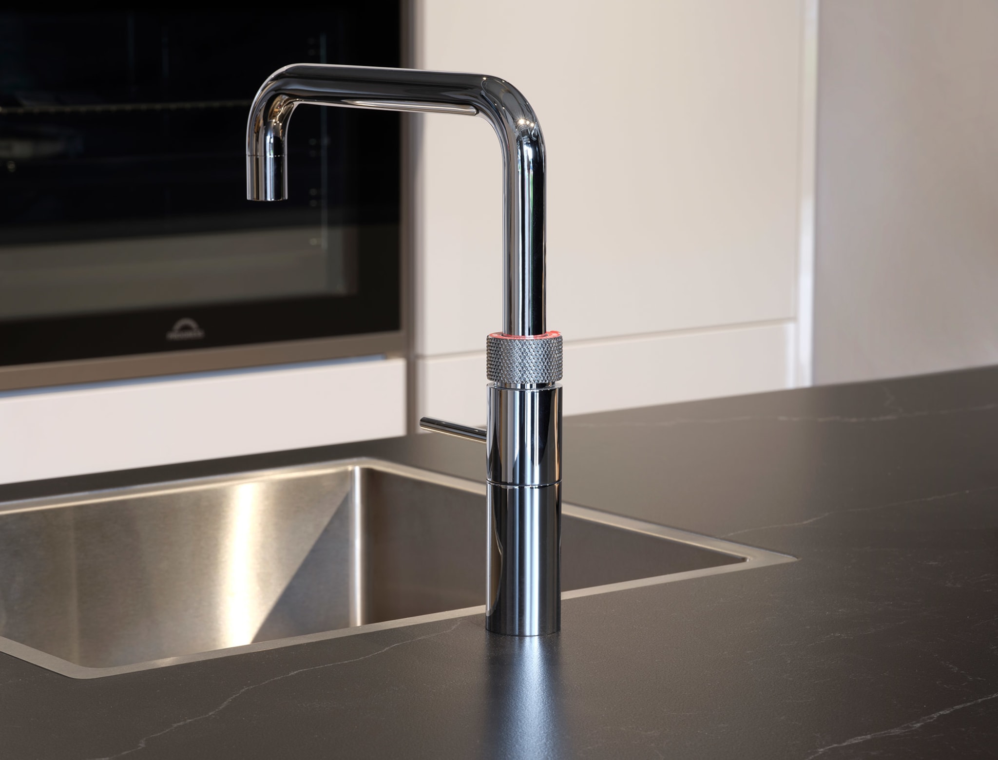 Een moderne Kitchen4All eilandkeuken met een donker composiet werkblad en een strakke chromen kraan.