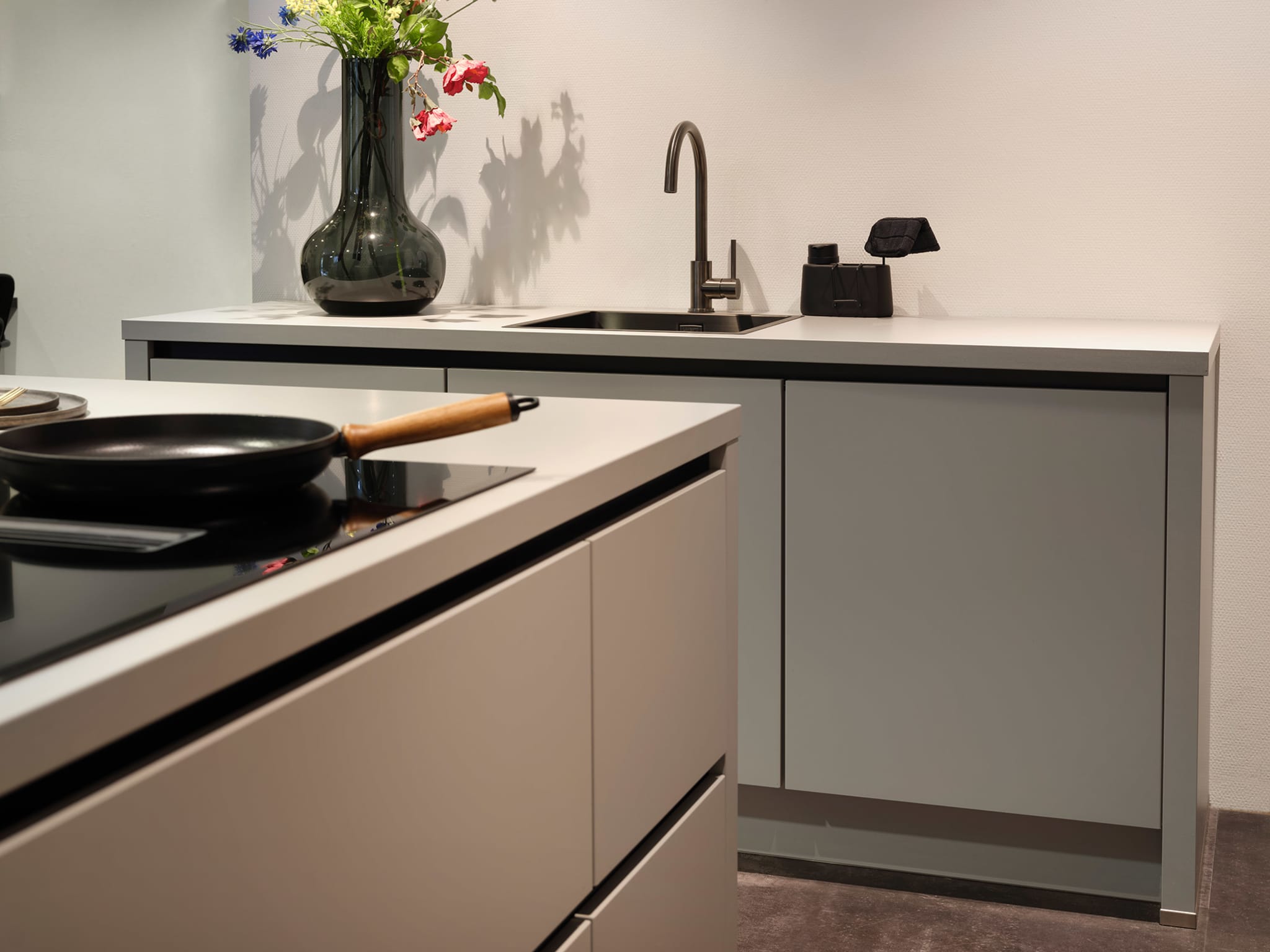 Moderne Kitchen4All eilandkeuken Structuur warm met matte grijze fronten, greeplijsten en een wit composiet werkblad.