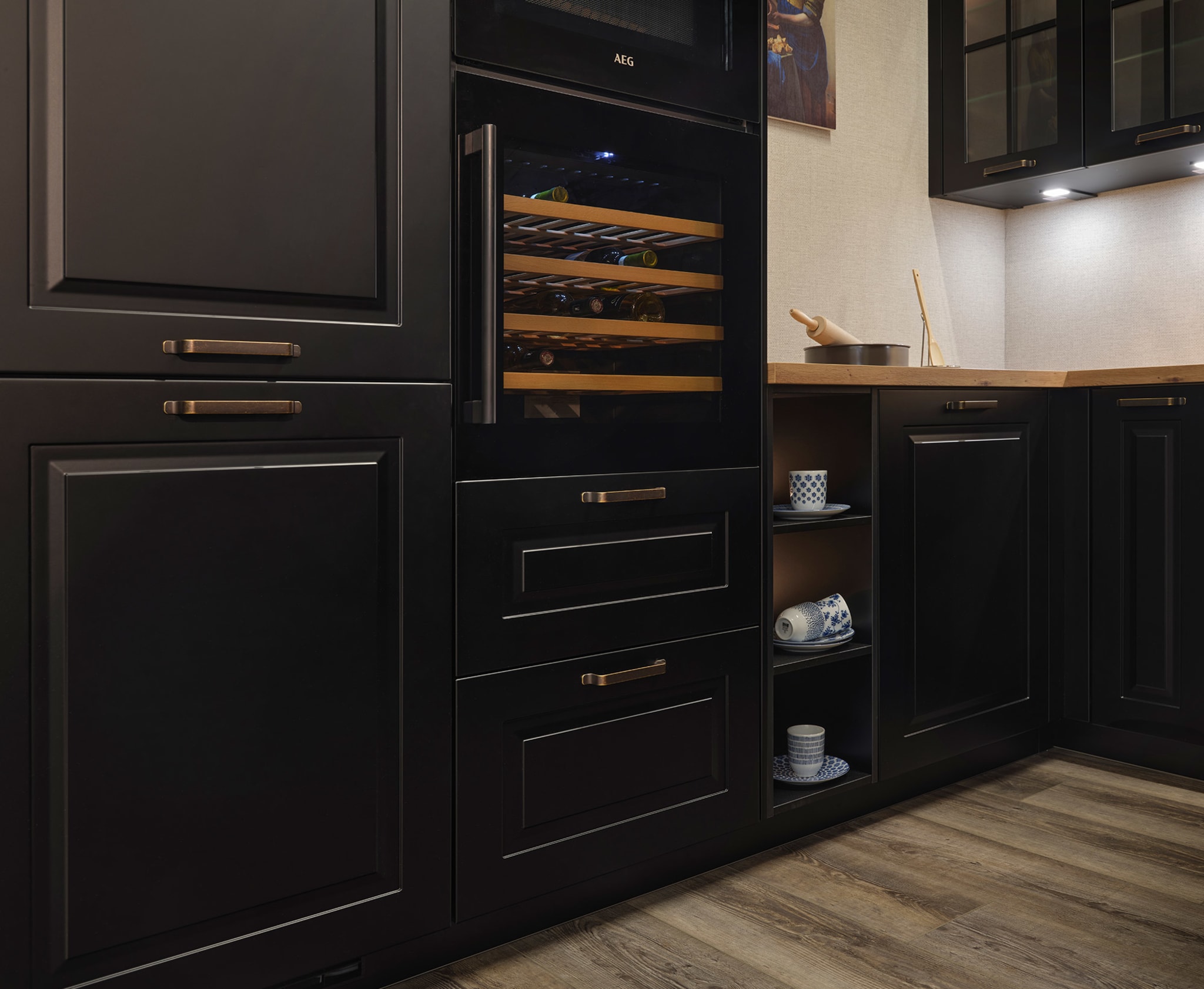 Een landelijke, zwarte L-keuken met kaderfronten, houten werkblad en geïntegreerde wijnklimaatkast.