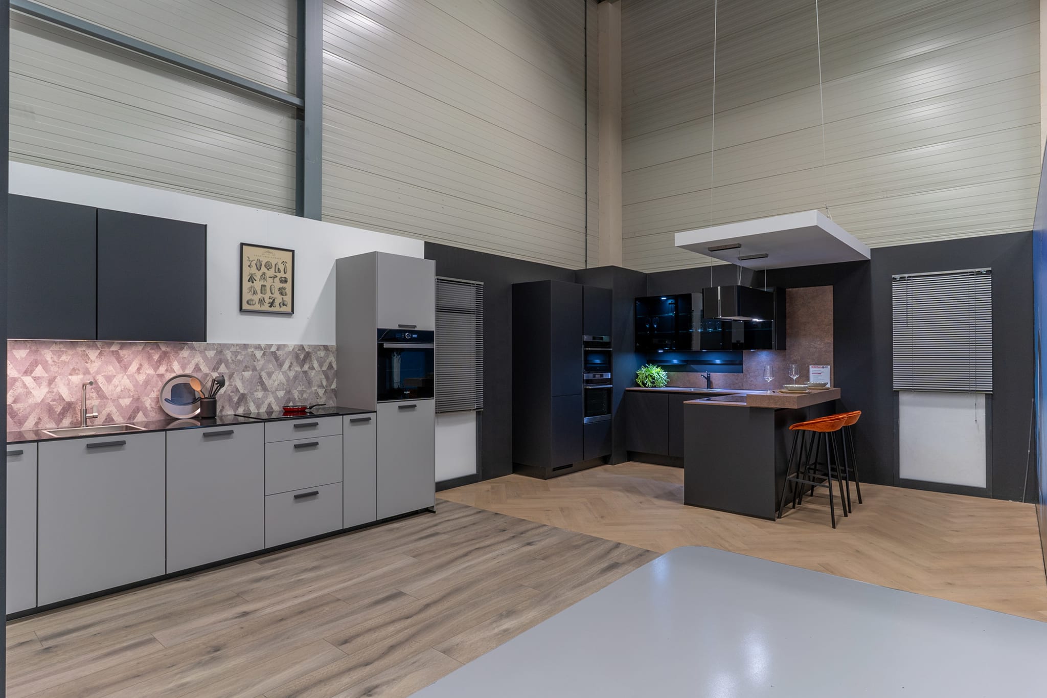 Grijze keukenopstellingen met kookeiland en barkrukken in de Kitchen4All-winkel