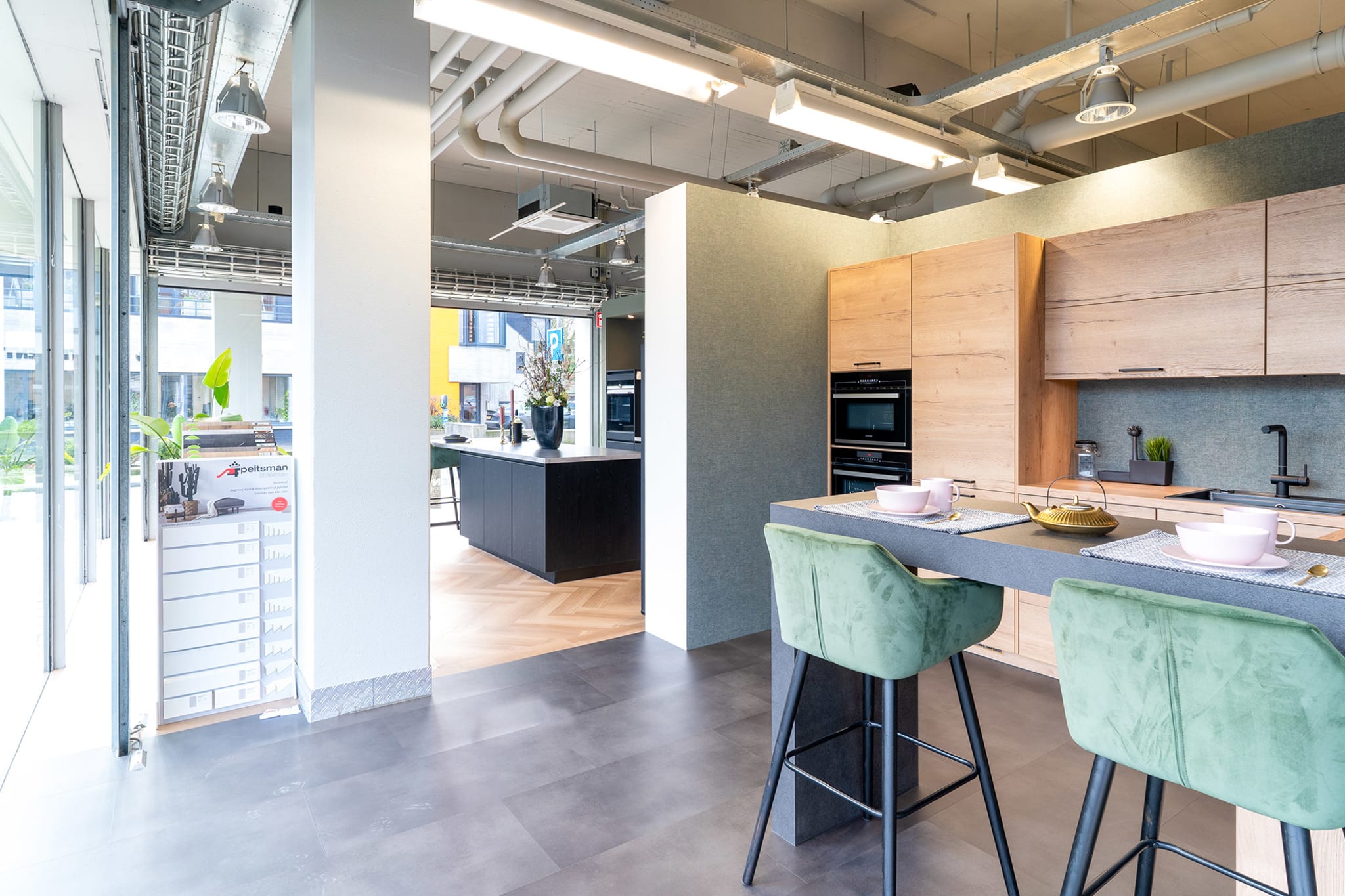 Gedekt bareiland met groene barkrukken en licht-eiken kastenwand in de Kitchen4All-winkel