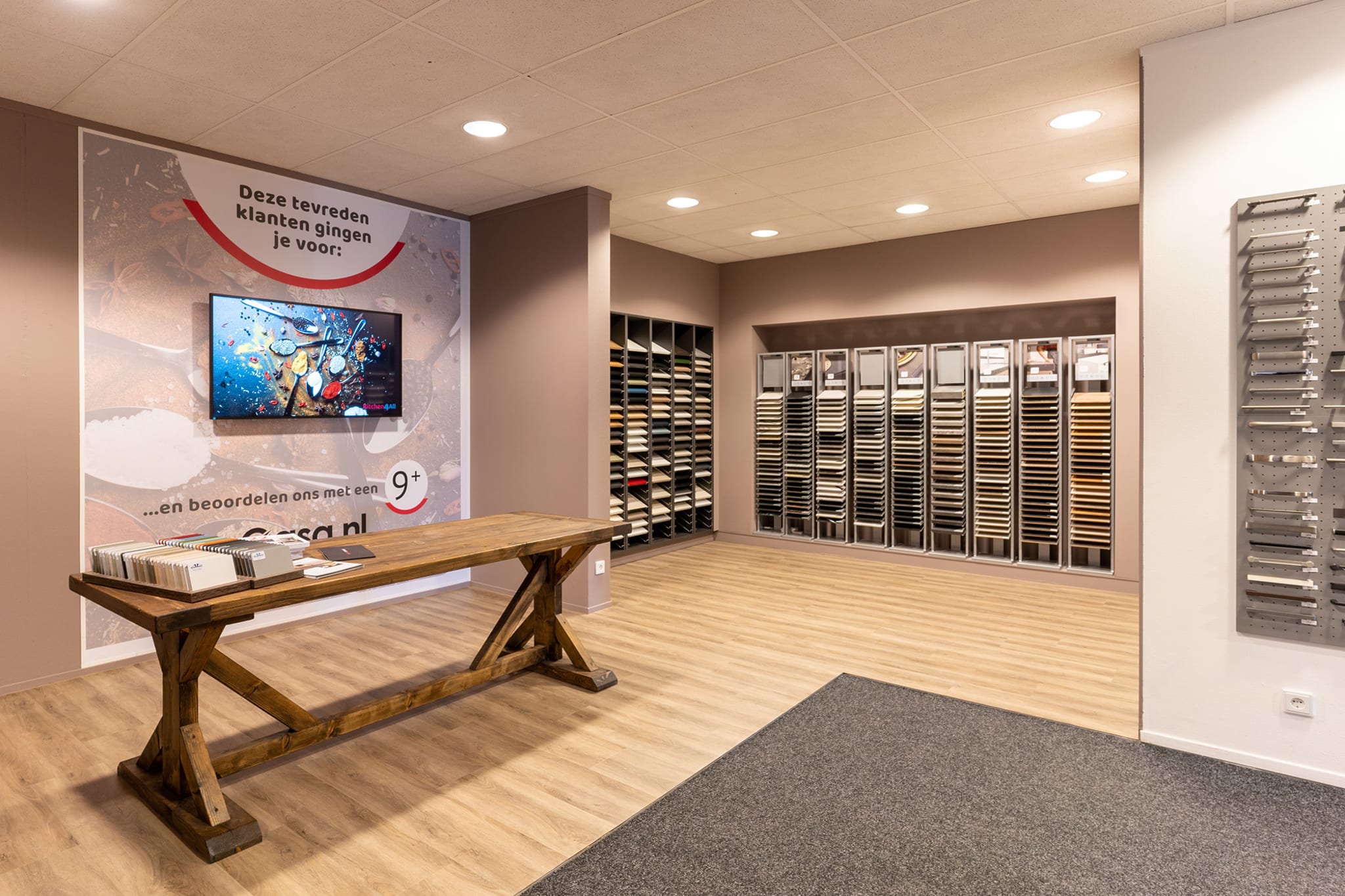 Stalenwand met fronten en werkbladen en een houten zitbank in de Kitchen4All-winkel