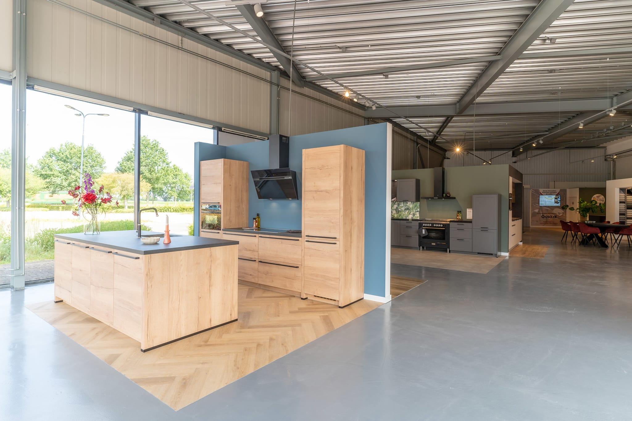 Lichte eiken keuken met kookeiland tegen een blauwe wand