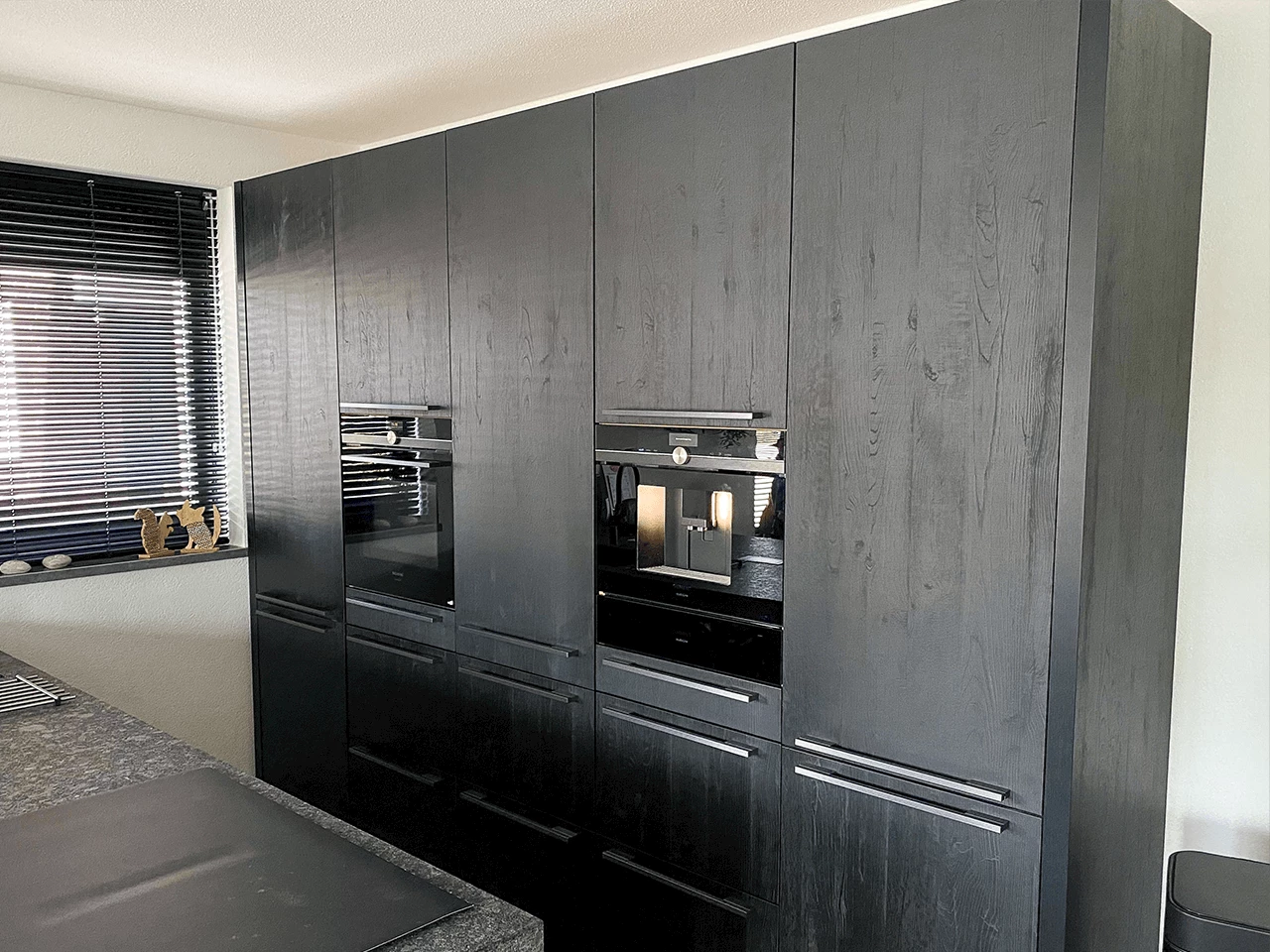 Matte zwarte kastenwand met houtnerf-fronten en inbouwapparatuur