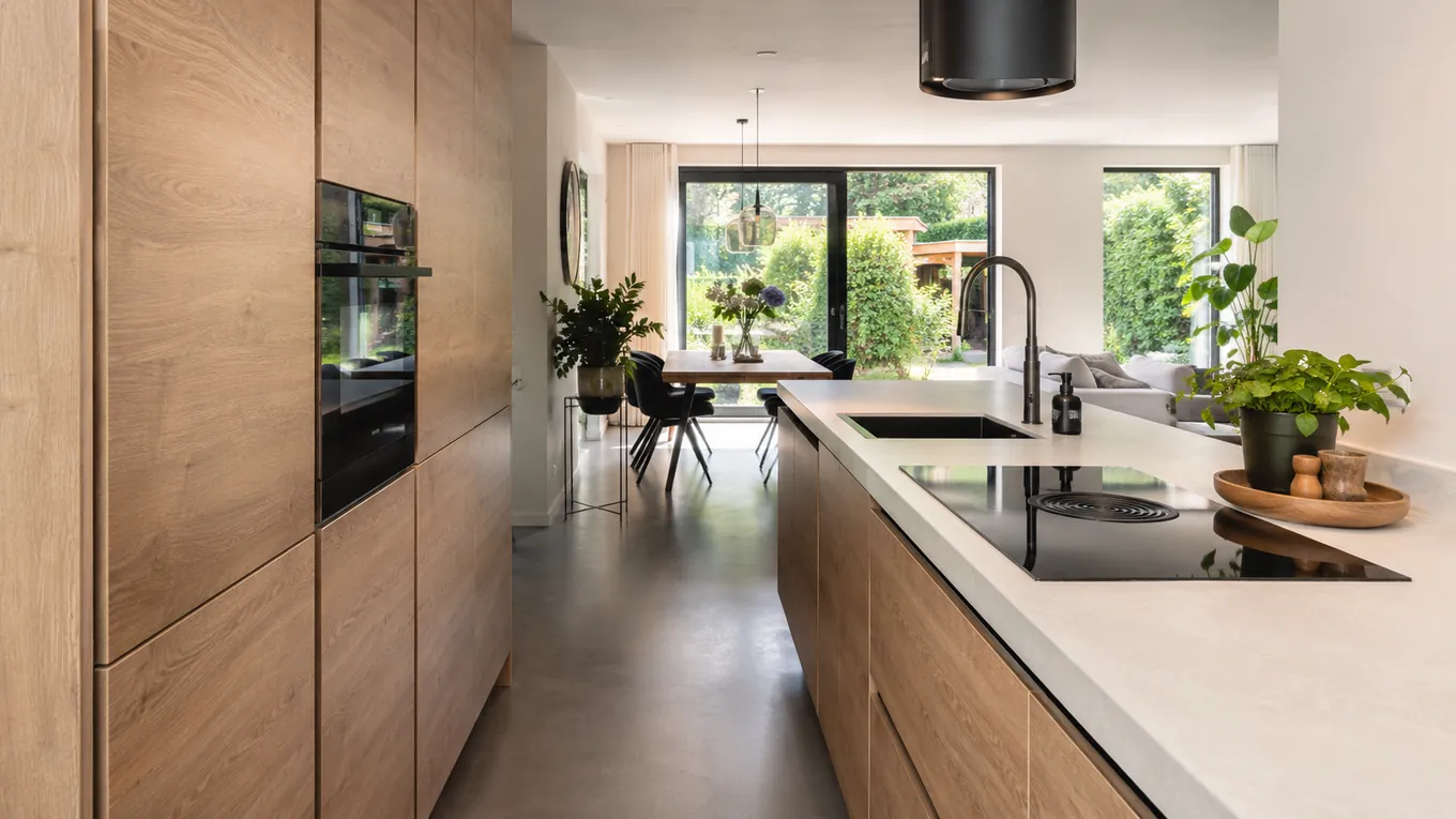 Moderne eiken keuken met greeploze fronten langs een wand en uitzicht op de tuin
